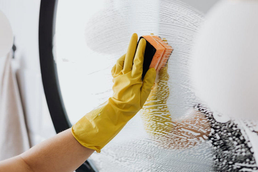 A professional cleaner wiping a mirror with a sponge.